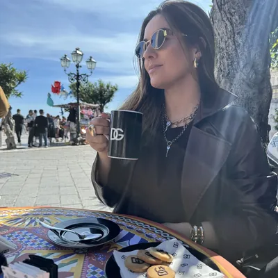 Carol Marcelino usando óculos, colares e anéis em um café.