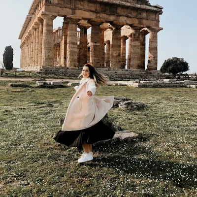 Carol Marcelino com casaco claro diante de um templo histórico europeu.